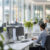 Beamte in eleganter Businesskleidung arbeiten konzentriert an weißen Schreibtischen in einem weitläufigen, lichtdurchfluteten Großraumbüro.